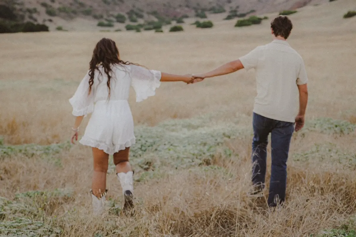 woman and man holding hand walking across field