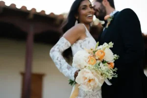 A couple at a wedding stand side by side, one holding a bouquet
